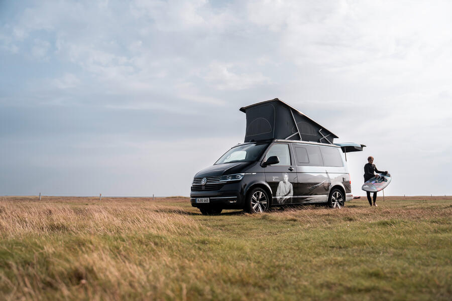 Ein Mann holte ein Surfbrett aus dem VW California Ocean