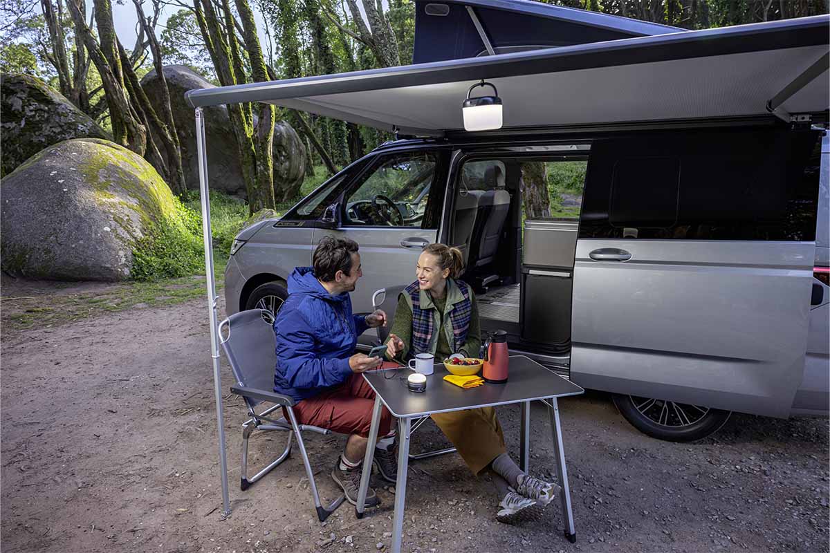 zwei Personen sitzen am Campertisch vor dem Camper