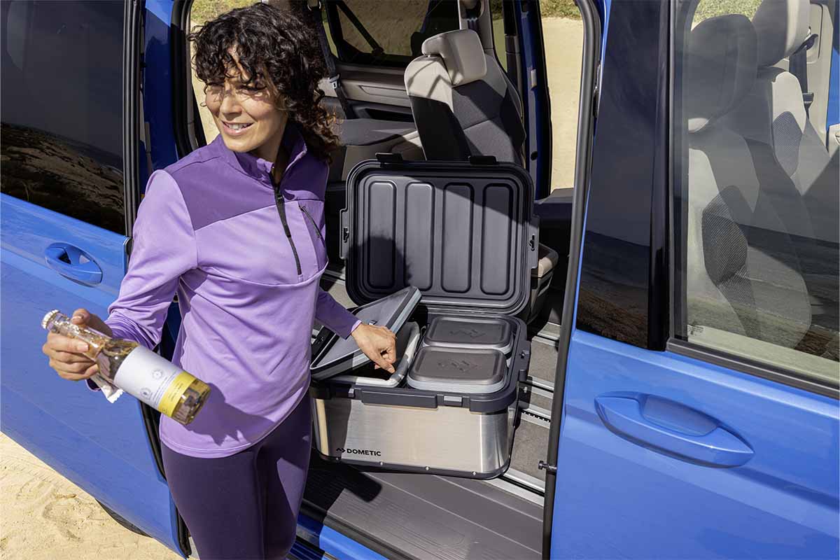 Frau mit einer Flasche steht vor einem Camper