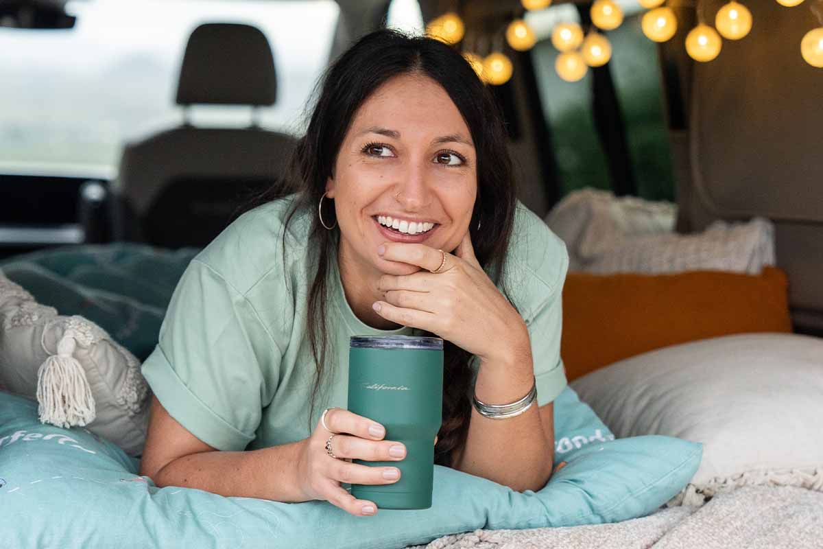 Eine Frau mit Thermobecher lacht aus dem Camper
