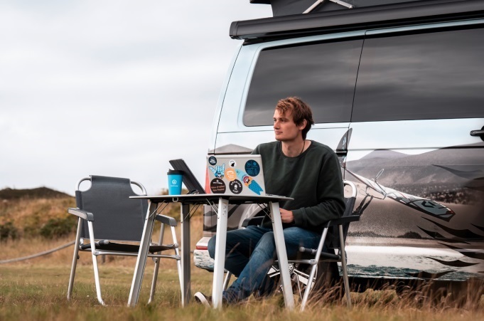 Ein Mann sitzt an einem VW California Ocean auf den Outdoormöbeln