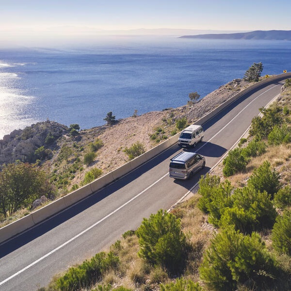 Zwei VW Wohnmobile kommen sich an einer Küstenstraße entgegen und man sieht das Meer im Hintergrund